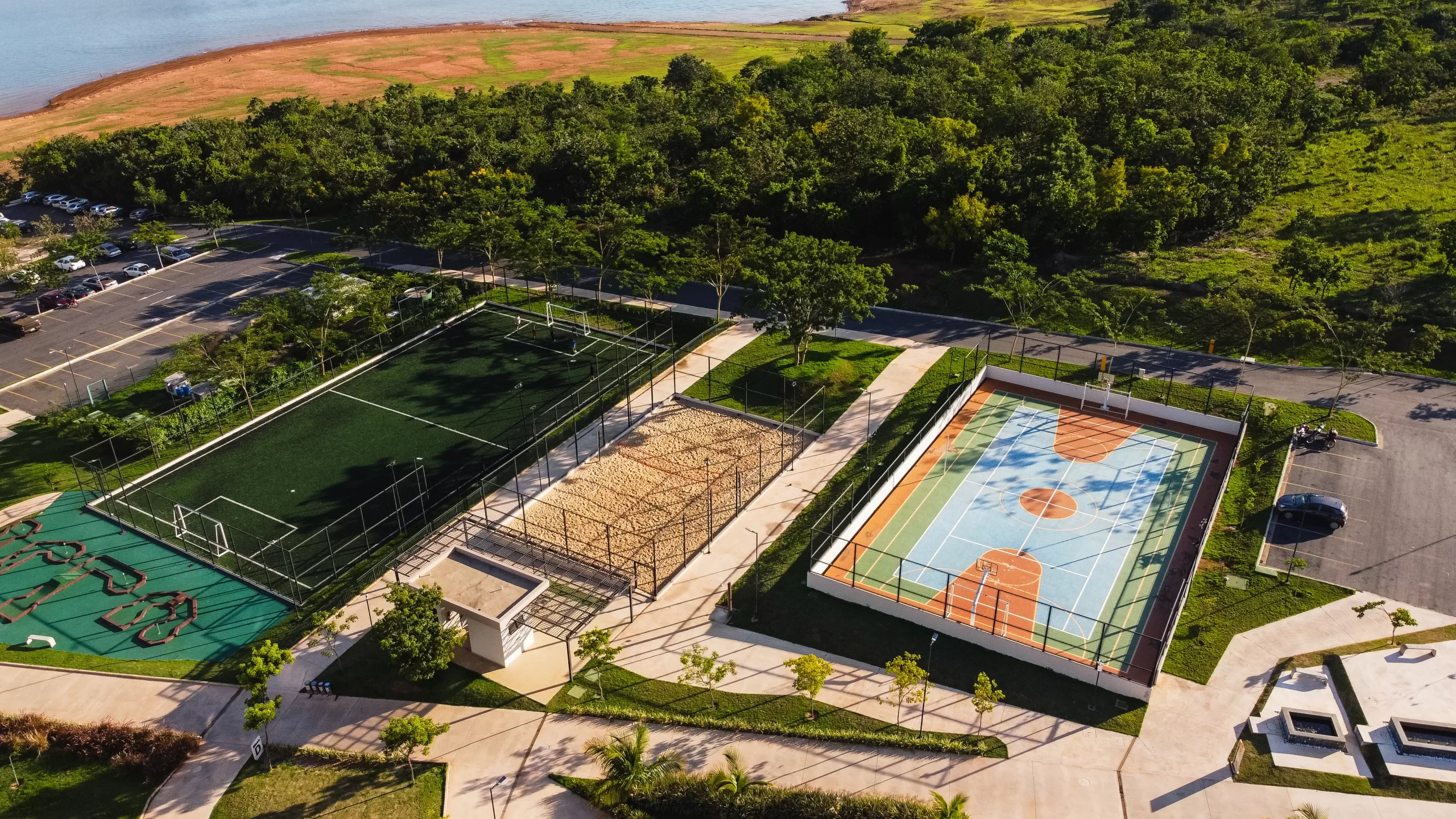 Vista aérea do complexo esportivo do Praias do Lago Eco Resort mostrando quadras de futebol, vôlei de areia, basquete e mini-golfe, com o Lago Corumbá ao fundo